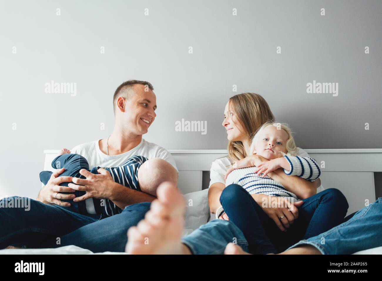 Happy family with two child have fun at home. Parents sit with their children on the bed and play with them Stock Photo