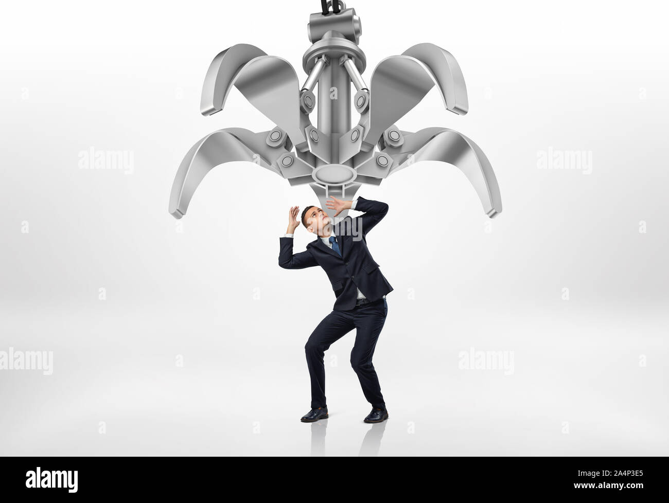Frightened businessman in protective pose looking up at giant mechanical claw above him Stock Photo