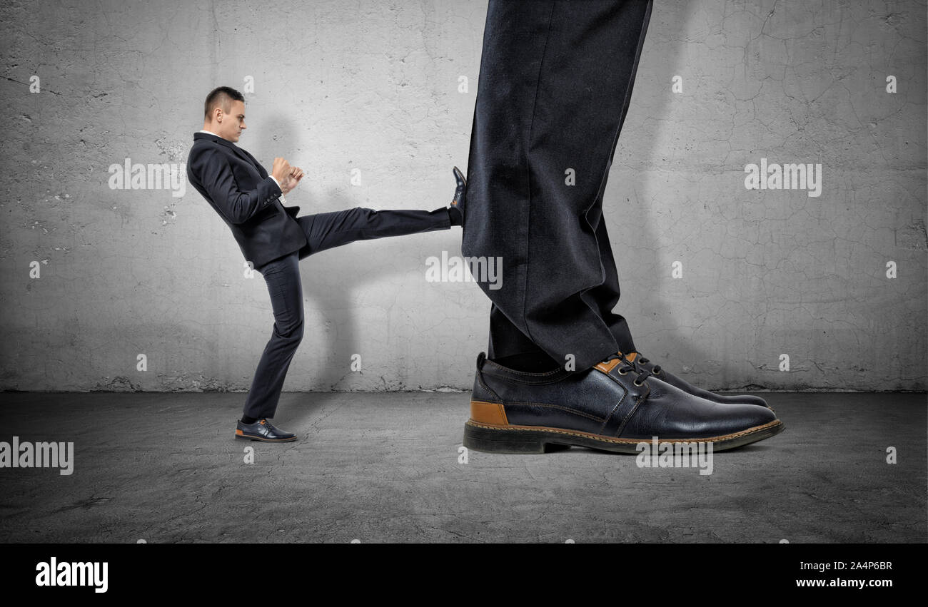 Tiny businessman kicking huge legs of another Stock Photo