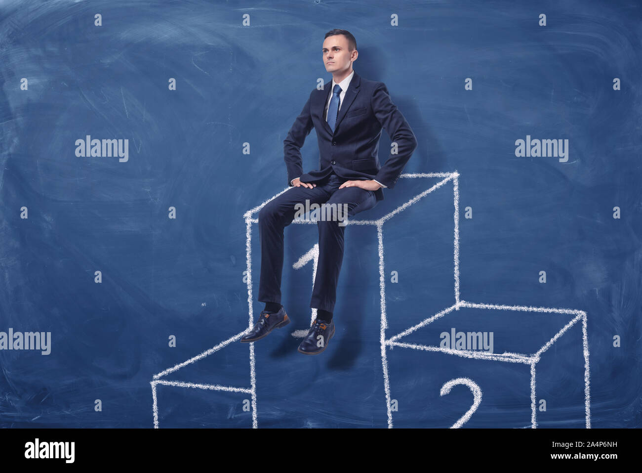 Businessman is sitting on the first place of a podium on blue blackboard background Stock Photo