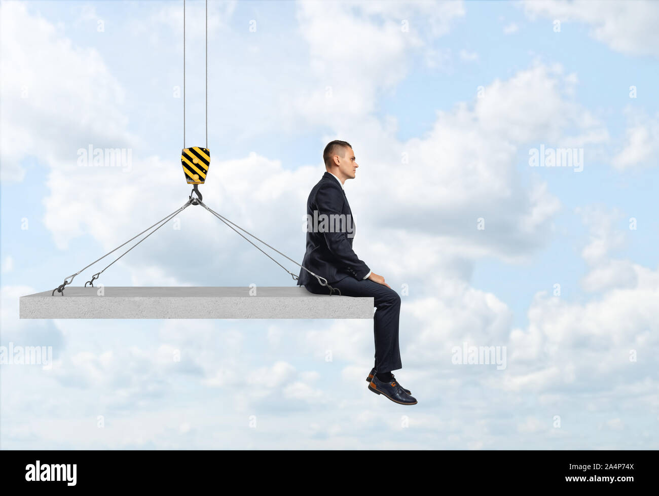 Businessman sitting on concrete slab suspended from construction crane hook. Stock Photo