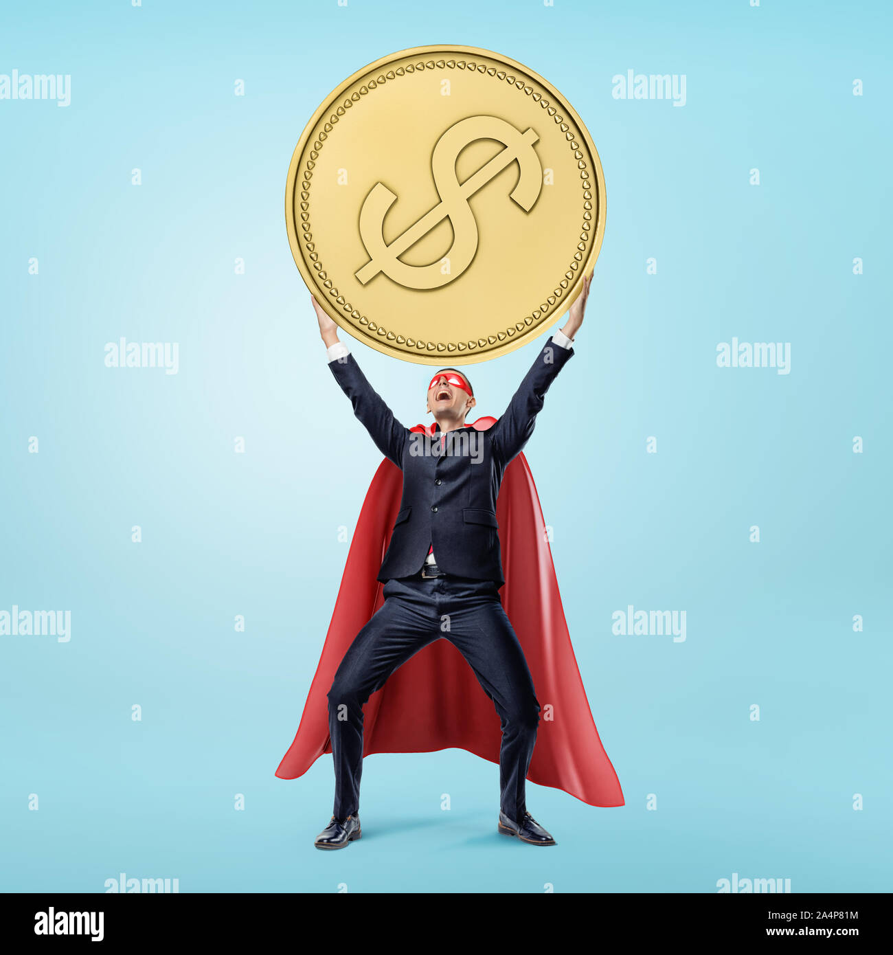 A businessman in a red flowing cape and a mask holding a huge golden coin in his hands in victory motion. Stock Photo