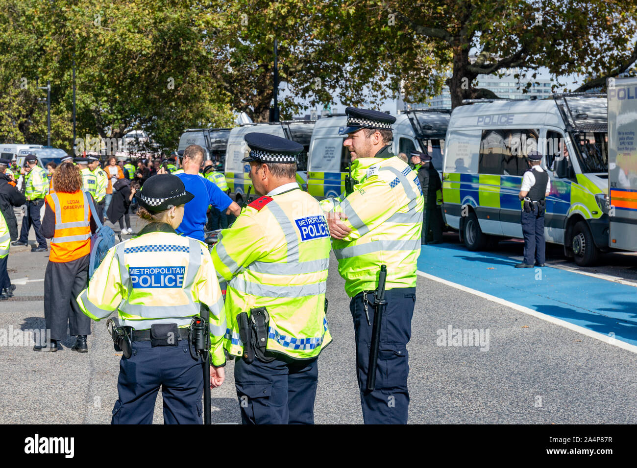 Millbank, London, UK 15th October 2019; Rear View of Three Police Officers at an Extinction Rebellion Protest With a Row of Police Vans in Background Stock Photo