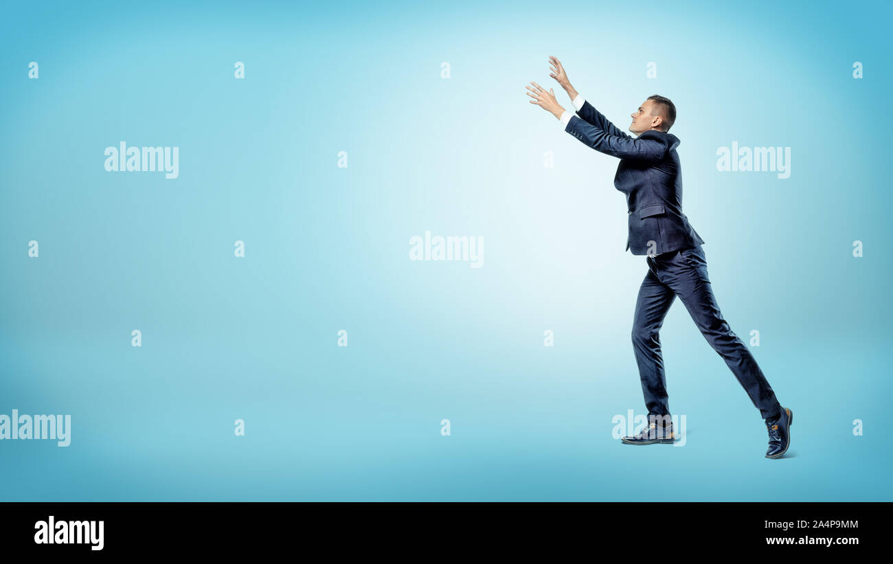 A businessman in side view with both hands raised up trying to catch something above. Stock Photo