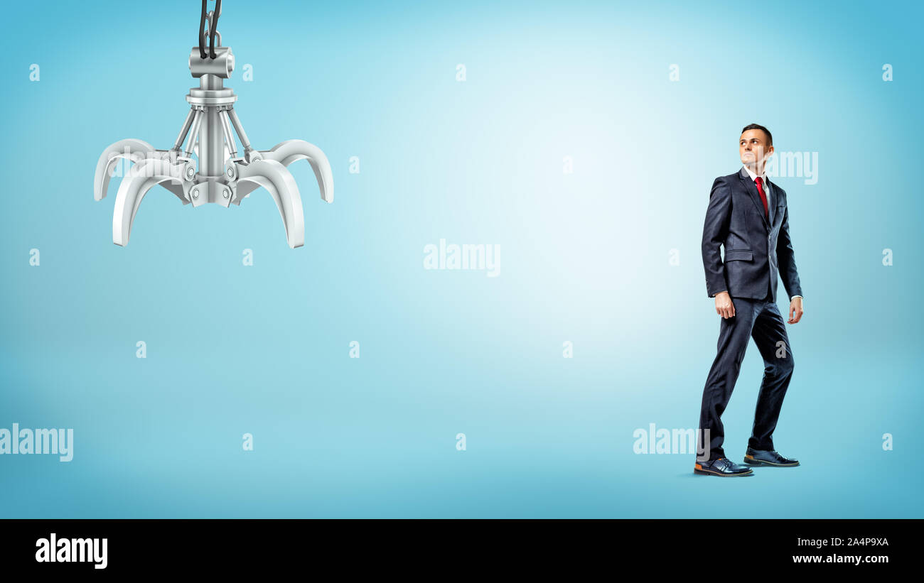 A businessman standing on blue background half-turned to look at a metallic robotic hand. Stock Photo
