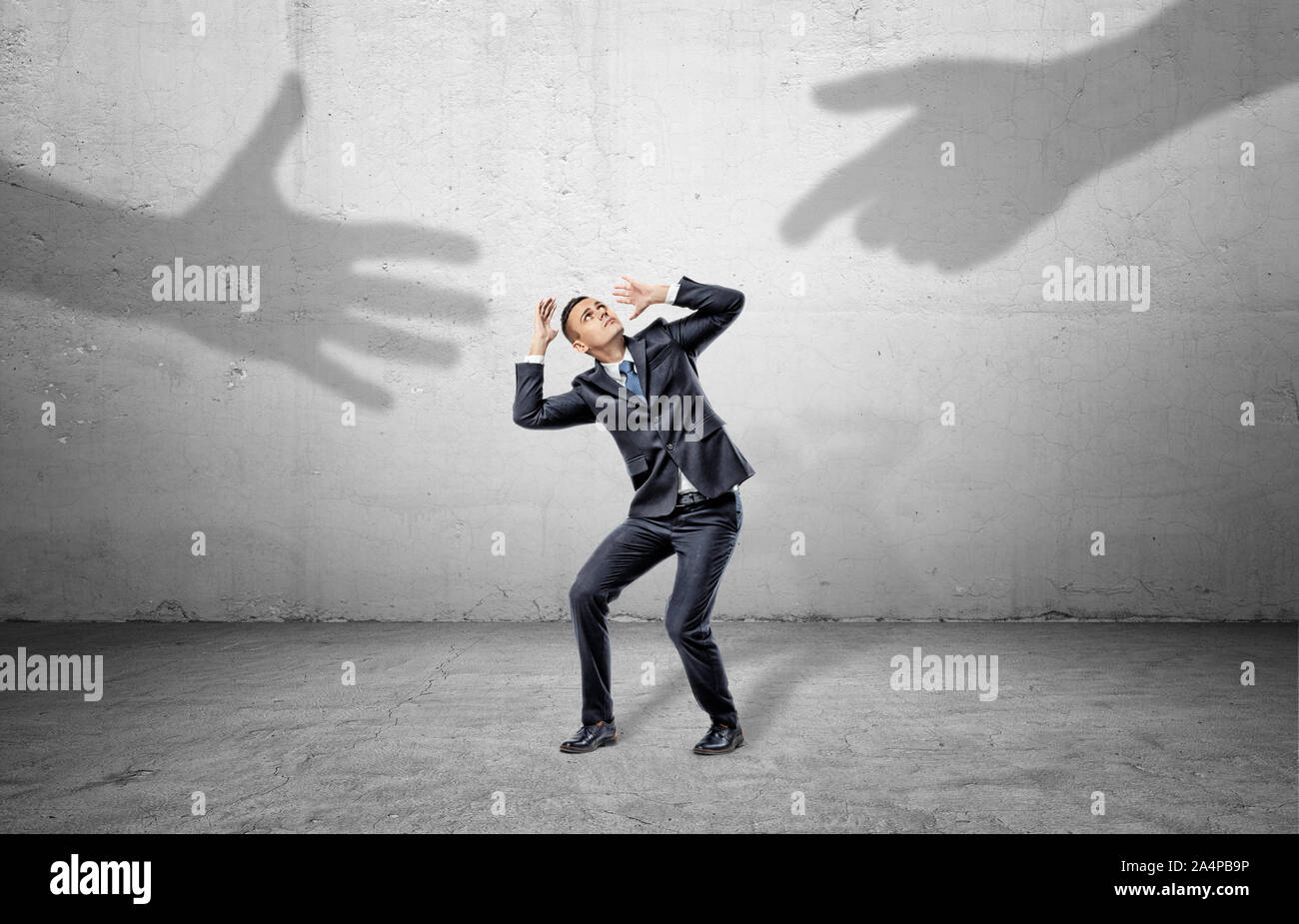 A scared businessman hides from two giant shadows of human hands ...