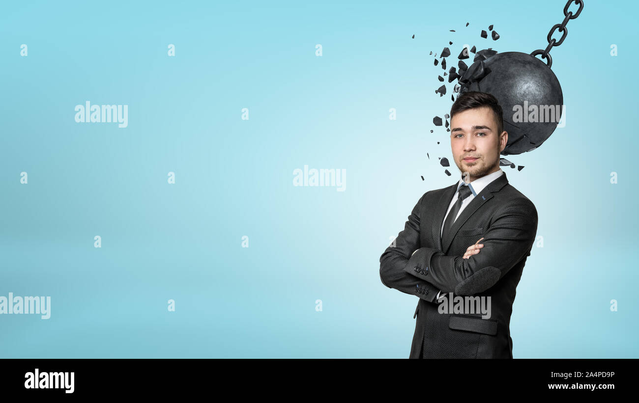 A bearded businessman stands with folded arms while a wrecking ball connects with his head. Stock Photo