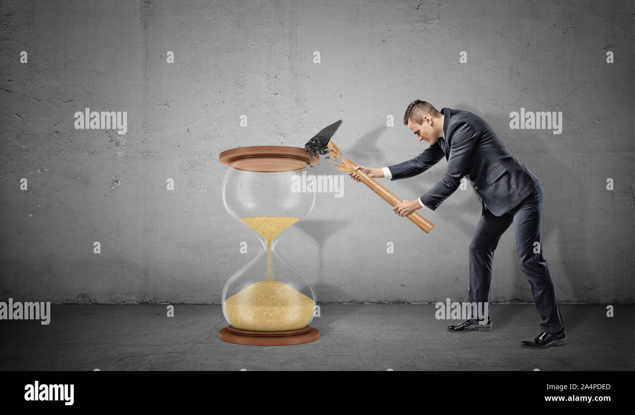 A businessman on concrete background tires to smash a large hourglass