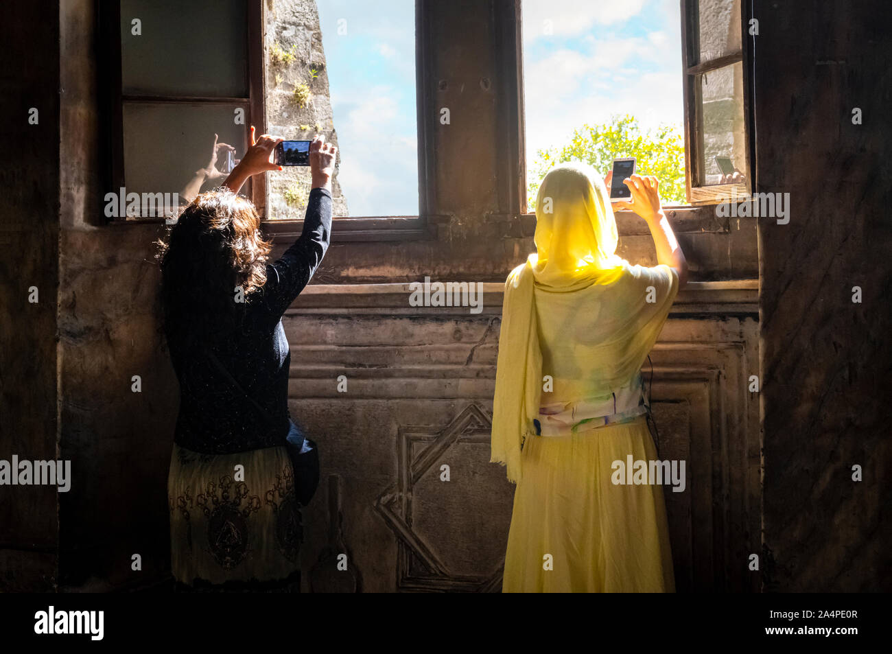 A muslim woman with traditional burqa abaya and a non-muslim woman take cell phone photographs out a window in the Hagia Sophia in Istanbul, Turkey Stock Photo
