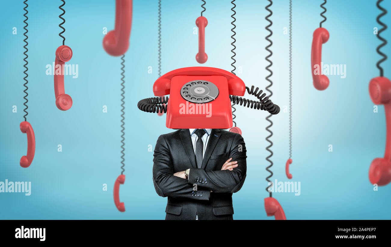 A businessman with folded arms stands surrounded by phone receivers and with one red retro phone placed on his head. Stock Photo