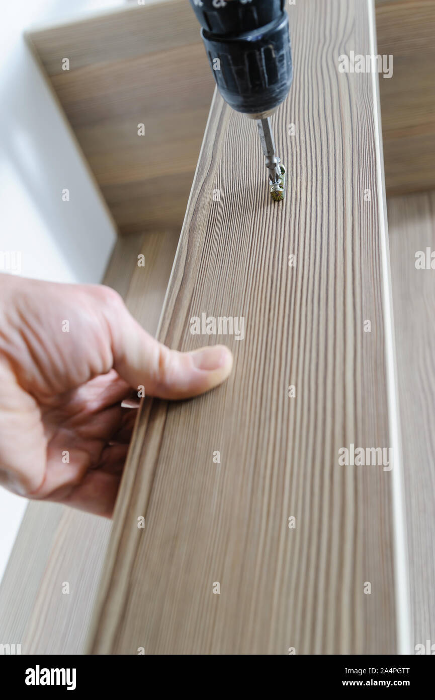 A man is installing a hook for clothes. He is using a screwdriver to fix the bracket hook. Stock Photo