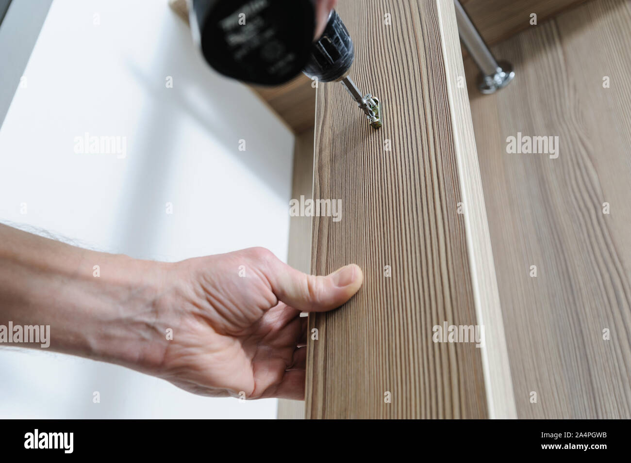 A man is installing a hook for clothes. He is using a screwdriver to fix the bracket hook. Stock Photo