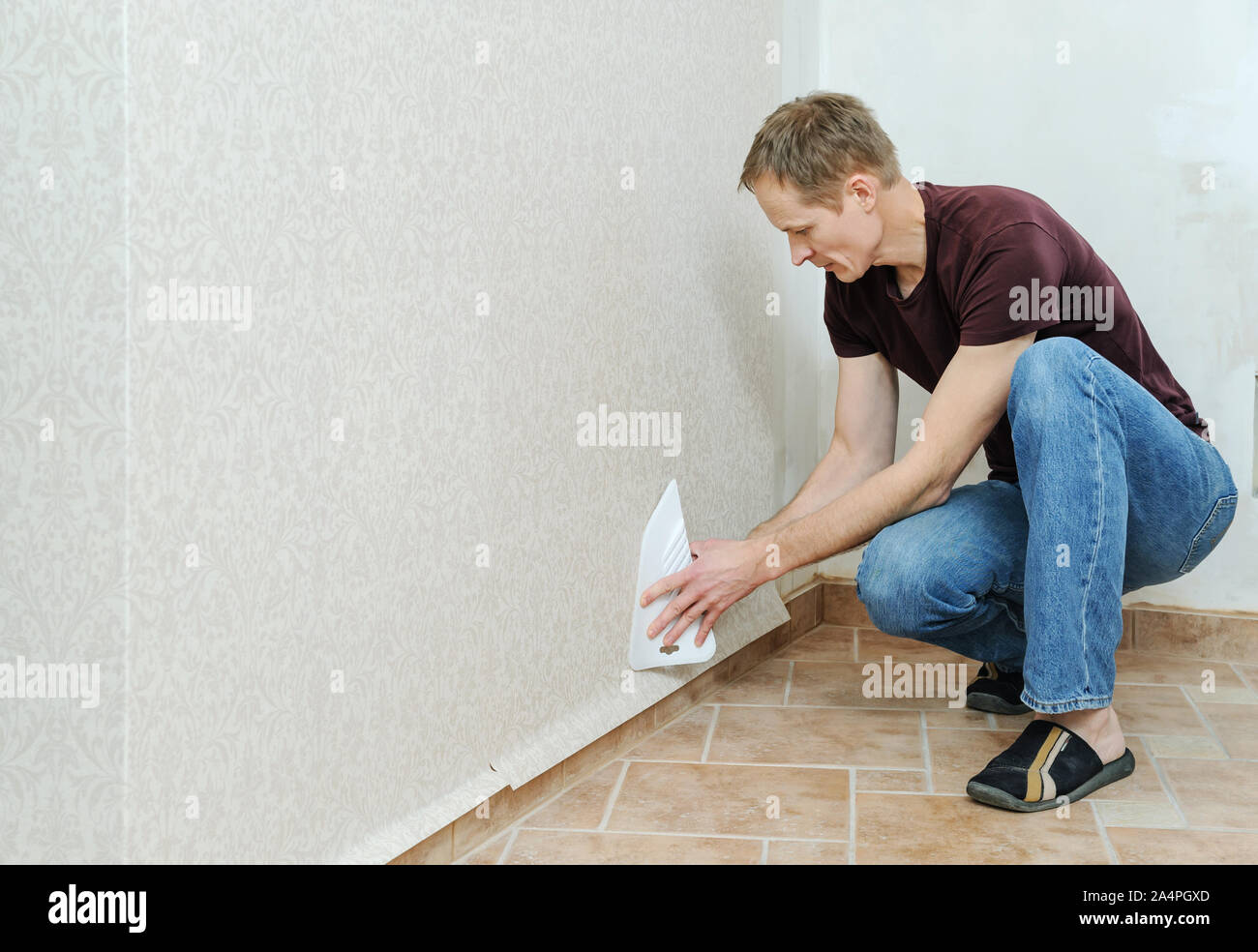 Glueing wallpapers at home. Man is using scraper to smoothing wallpapers on the wall Stock Photo