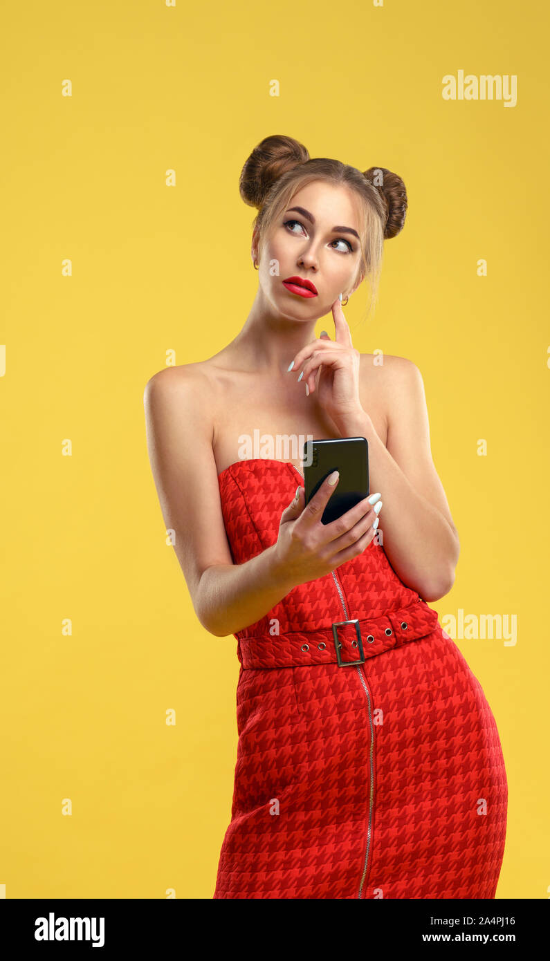 Girl in Red off shoulder dress holding a smartphone looking up and thinking Stock Photo