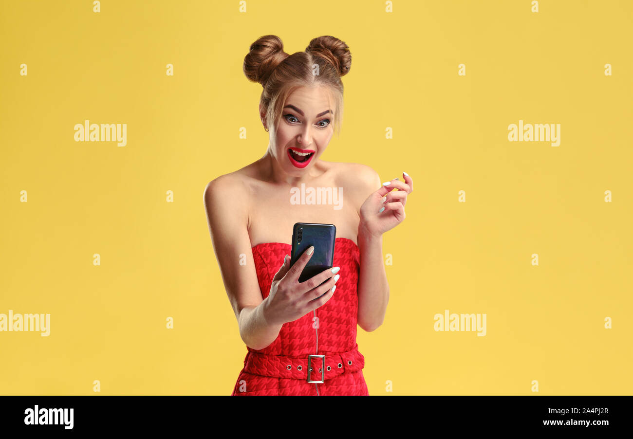 Studio shot of Surprised girl looking at smartphone on isolated yellow background Stock Photo