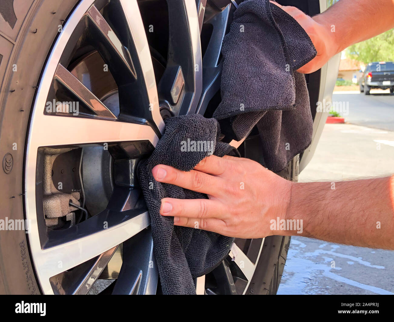 Man's hand cleaning wheel and tire with black microfiber cloth. Hand