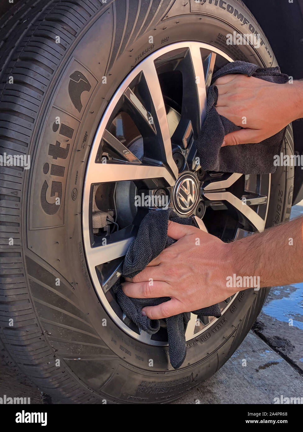 Man's hand cleaning wheel and tire with black microfiber cloth. Hand