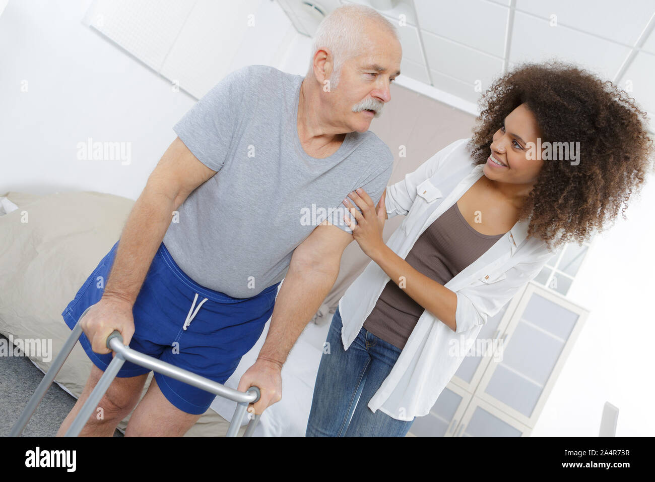 carer helping senior man walk with frame Stock Photo