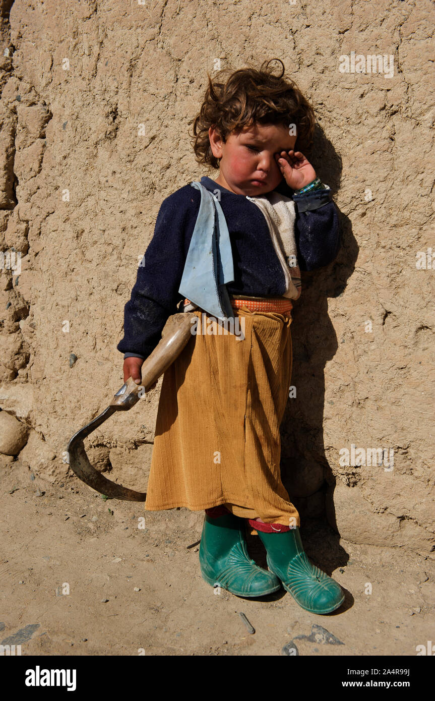 A little Afghan girl holds a sickle in her hand outside her house, in the village of Bam Sara,i in the central Bamyan Province, Afghanistan. May 12, 2009. Stock Photo