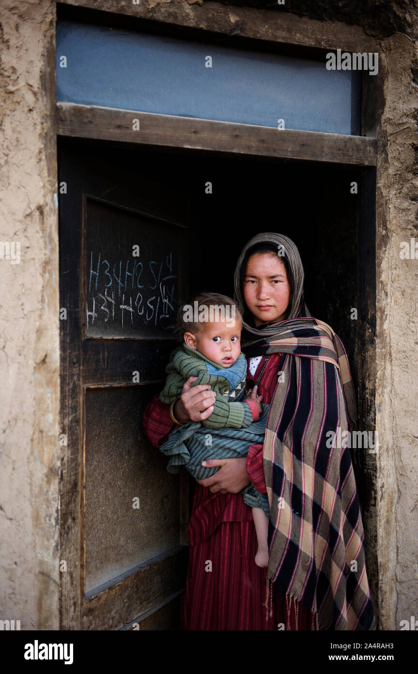 A girl carries a baby and stands at the doorway of her house in the village of Rag-e-shad on the outskirts of the city of Bamyan in the central Bamyan Province. Afghanistan. May 11, 2009. Stock Photo