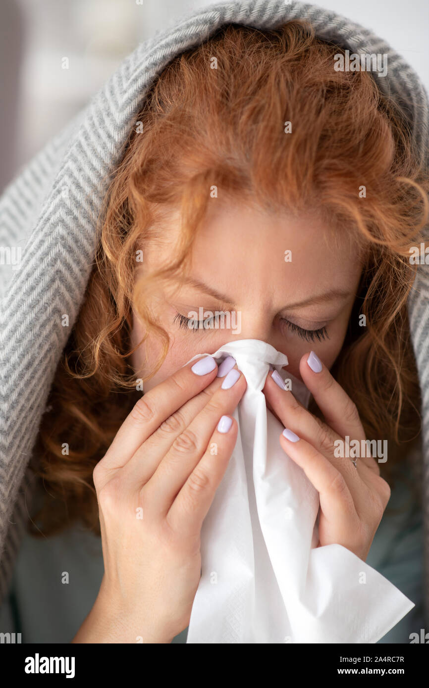 Woman covered in plaid taking napkin while having stuffy nose Stock Photo
