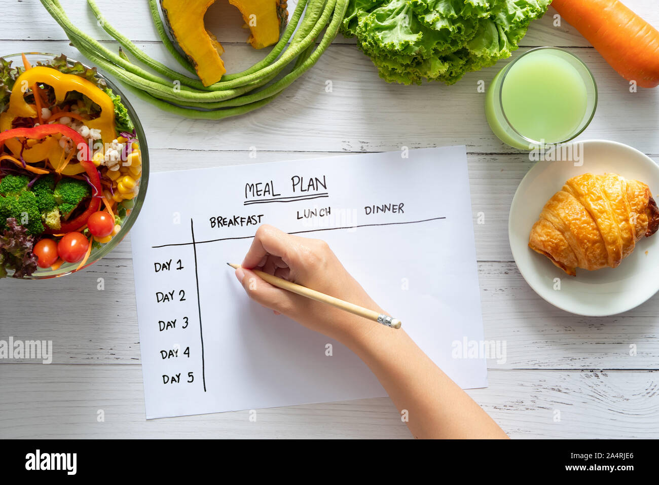 Calories control, meal plan, food diet and weight loss concept. top view of hand filling meal plan on weekly table with salad and fresh vegetable on d Stock Photo