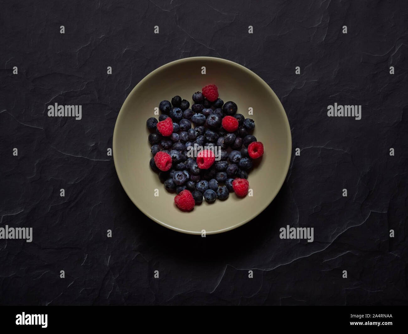 Blueberries and Raspberries in a cream dish on a black background in studio viewed from above, flatlay concept Stock Photo