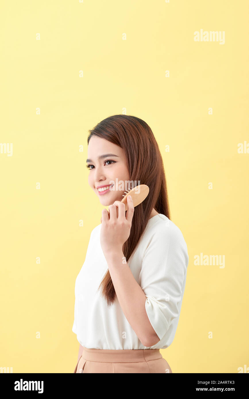 Portrait of cute young woman on yellow background combing hair. Stock Photo