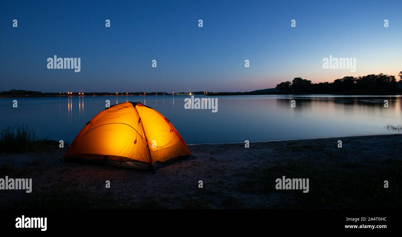 Orange interior lit tent on a lake at dusk Stock Photo
