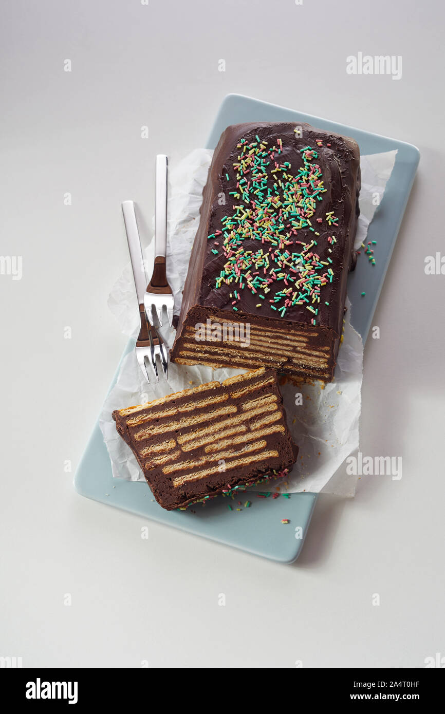 Top view of chocolate cake with biscuits and colorful topping, served with two forks on blue ceramic tray and white paper. Traditional uncooked Kalter Stock Photo