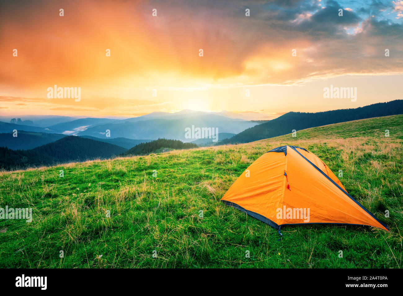 Orange tent in the mountains at sunset Stock Photo