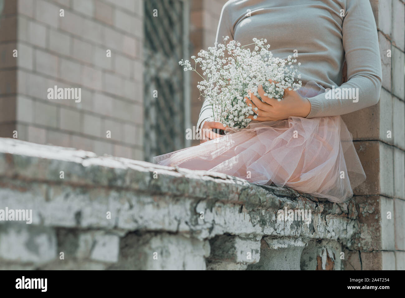 Woman in pink lace skirt with white flowers bouquet in her hands is sitting on stairs. Stock Photo