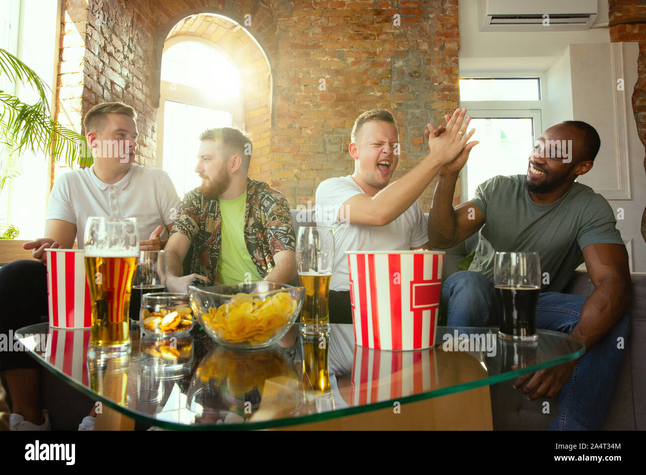 Group of excited friends playing video games at home. Male gamers or fans spending time and having fun together at home. Emotional, expressive, exciting gameplay. Modern tech, friendship, weekend. Stock Photo