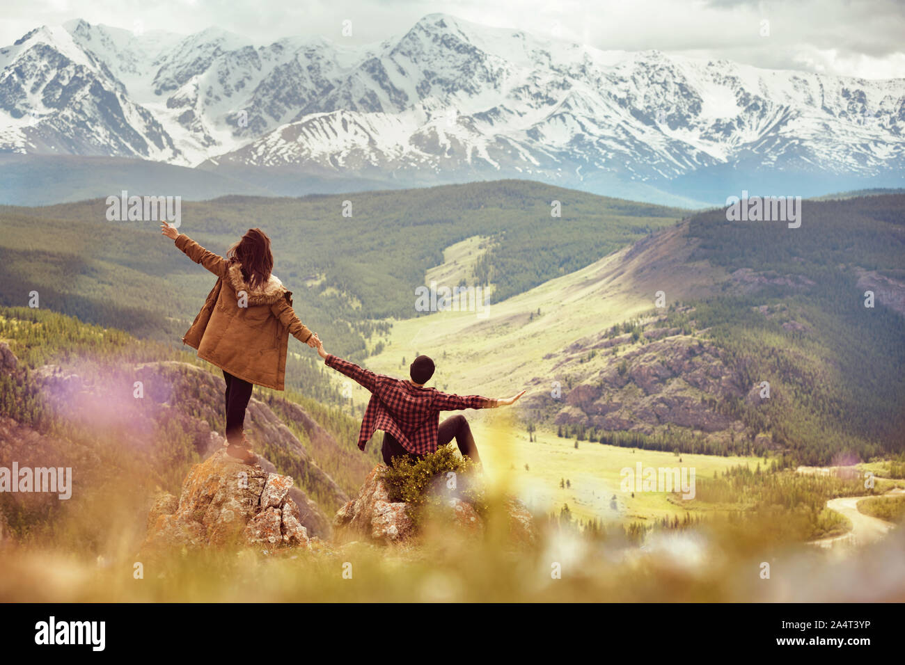 Happy couple with raised arms is having fun on view point in mountains Stock Photo