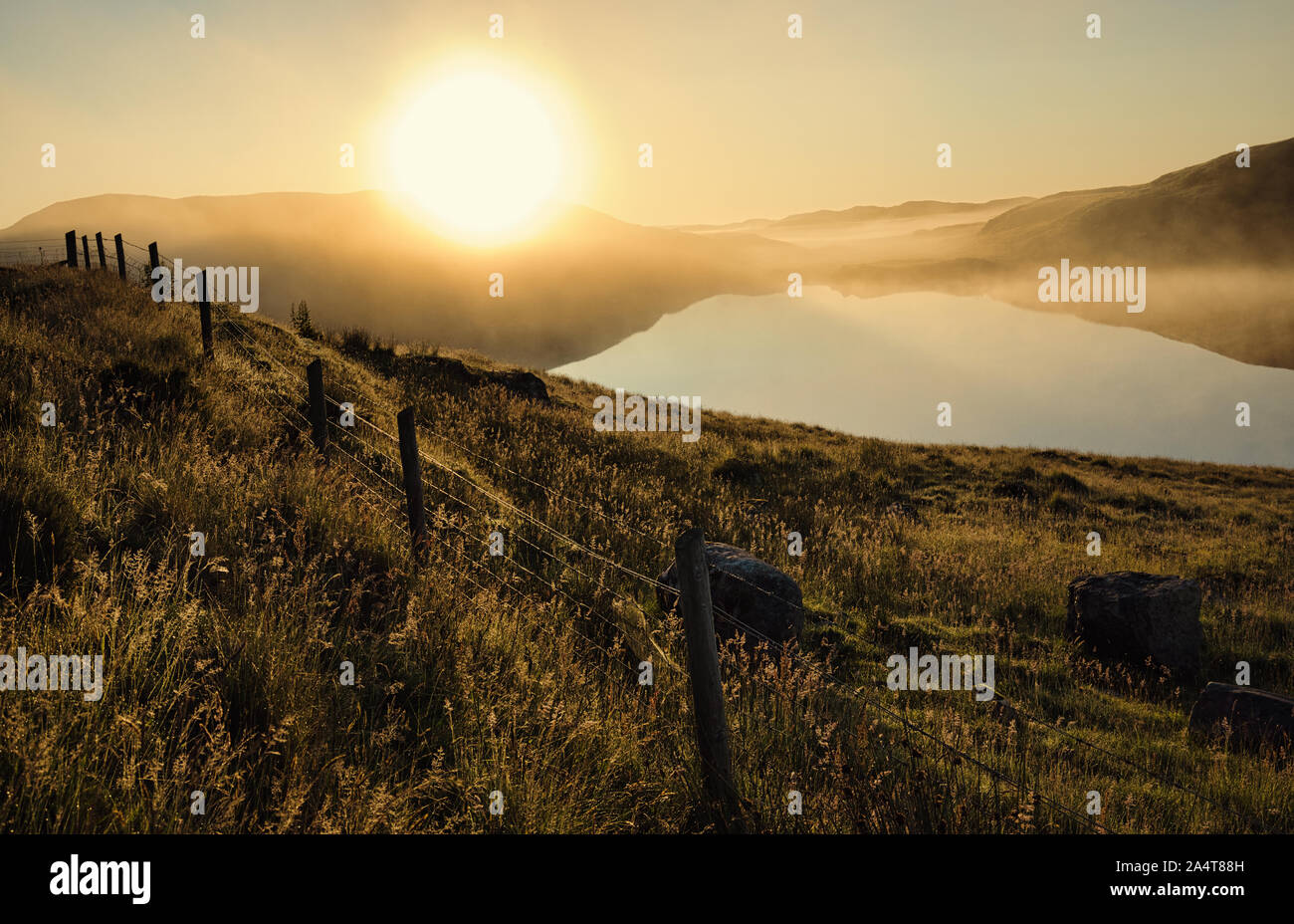 Summer dawn landscape with reflection in loch, dew and barbed wire fence, Isle of Harris, Outer Hebrides, Scotland Stock Photo