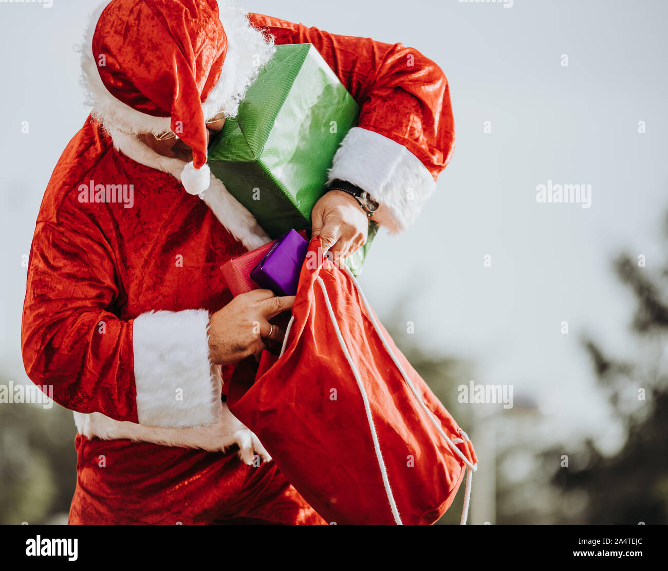 Stock photo of Santa Claus without beard standing putting presents in a red bag. Christmas time ...