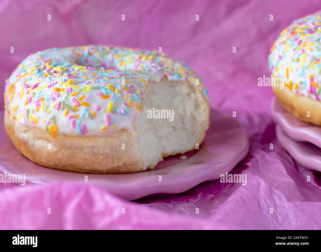 head on image  colorful sprinkles doughtnut   on a plate with a bite taken out Pink background for copy space Stock Photo
