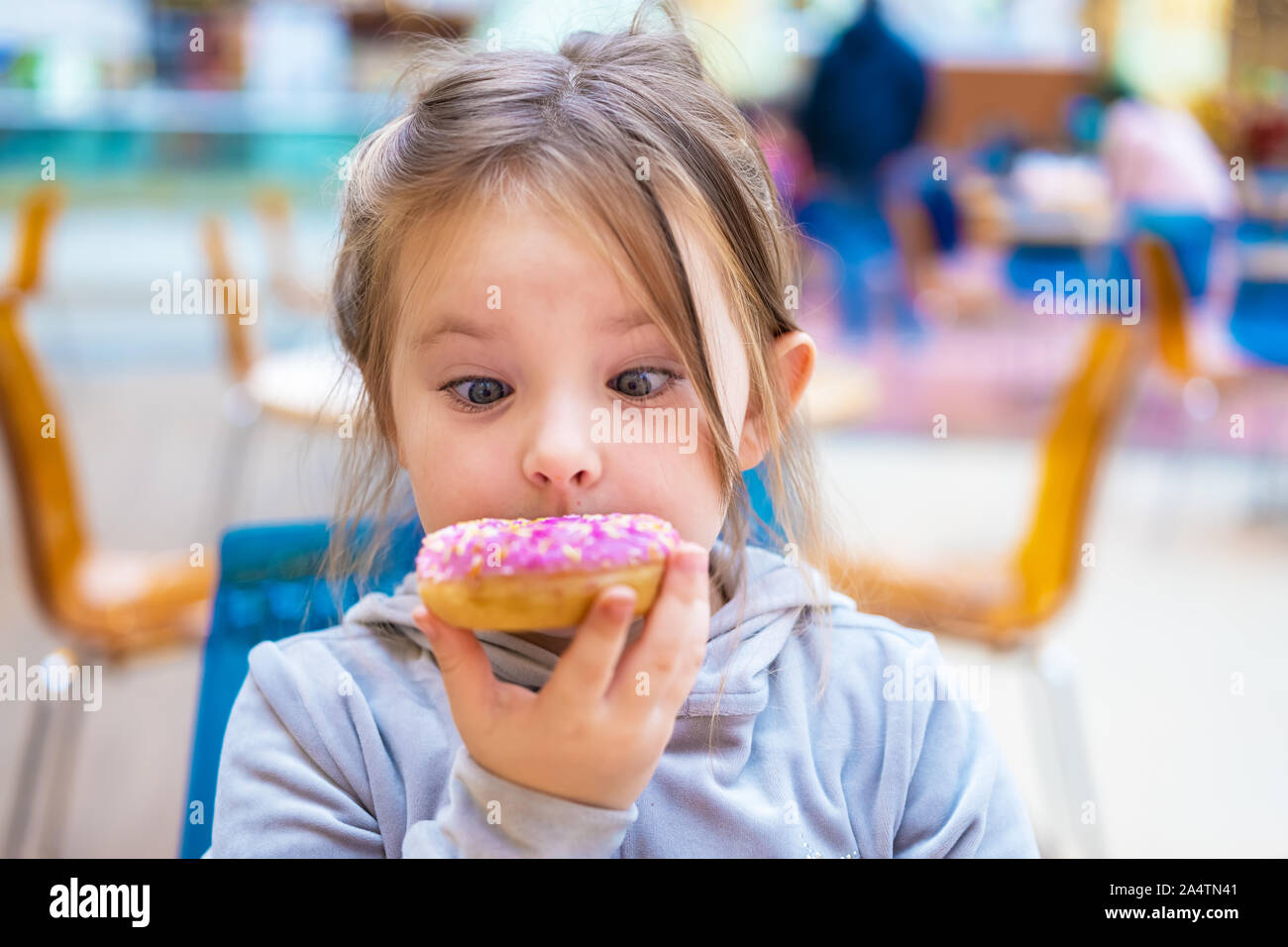 Cute girl eating a donut in a cafe. Funny portrait of a child Stock Photo