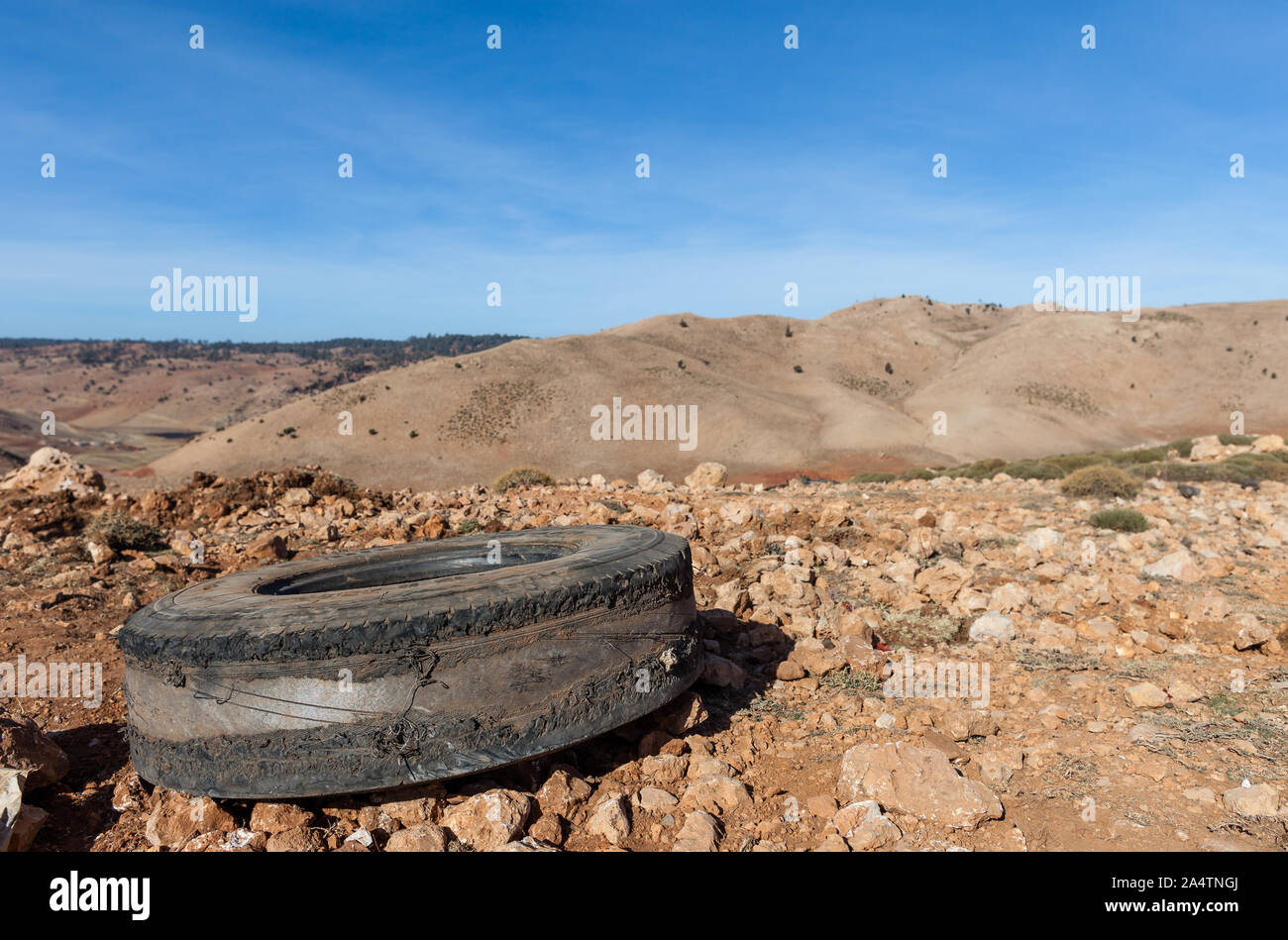 Old blown and worn out tire lying in the dirt and gravel beside a road in Morocco. Some hills are visible in the background. Stock Photo