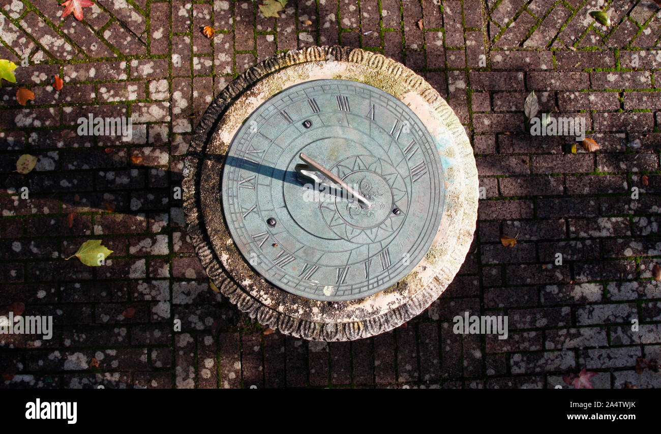 Top down photo of a stone and metal sundial on a mottled brick garden path Stock Photo