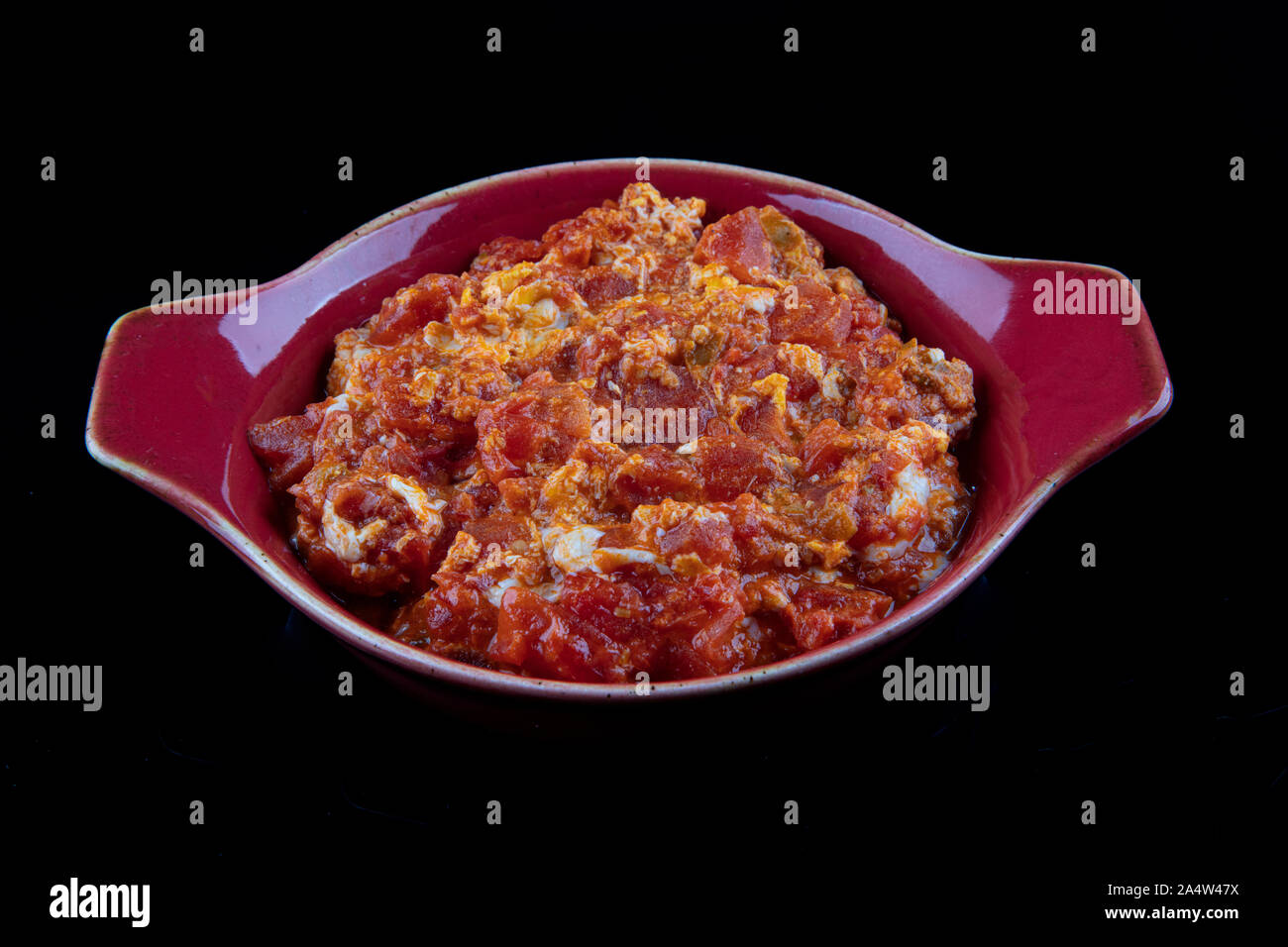 Turkish style Menemen on black background. Served on a red porcelain plate. Stock Photo