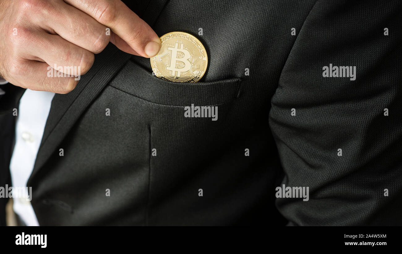 Businessman placing a Bitcoin in his jacket pocket in a close up view on his fingers and the coin. Stock Photo