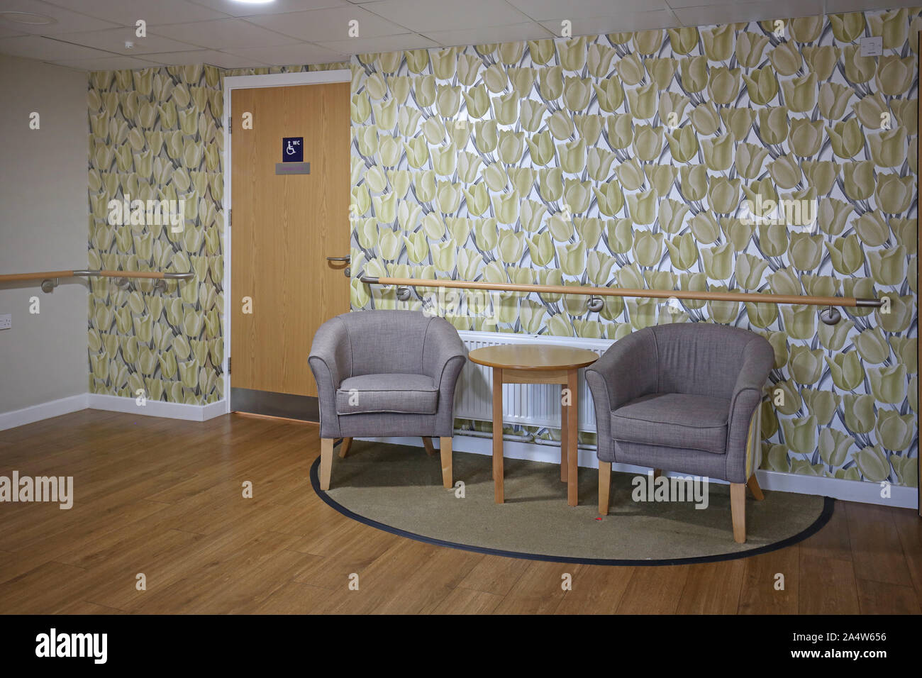 Interior of a newly refurbished care home near Wakefield, UK. Shows corridor seating area with bright wallpaper, armchairs and safety handrails. Stock Photo