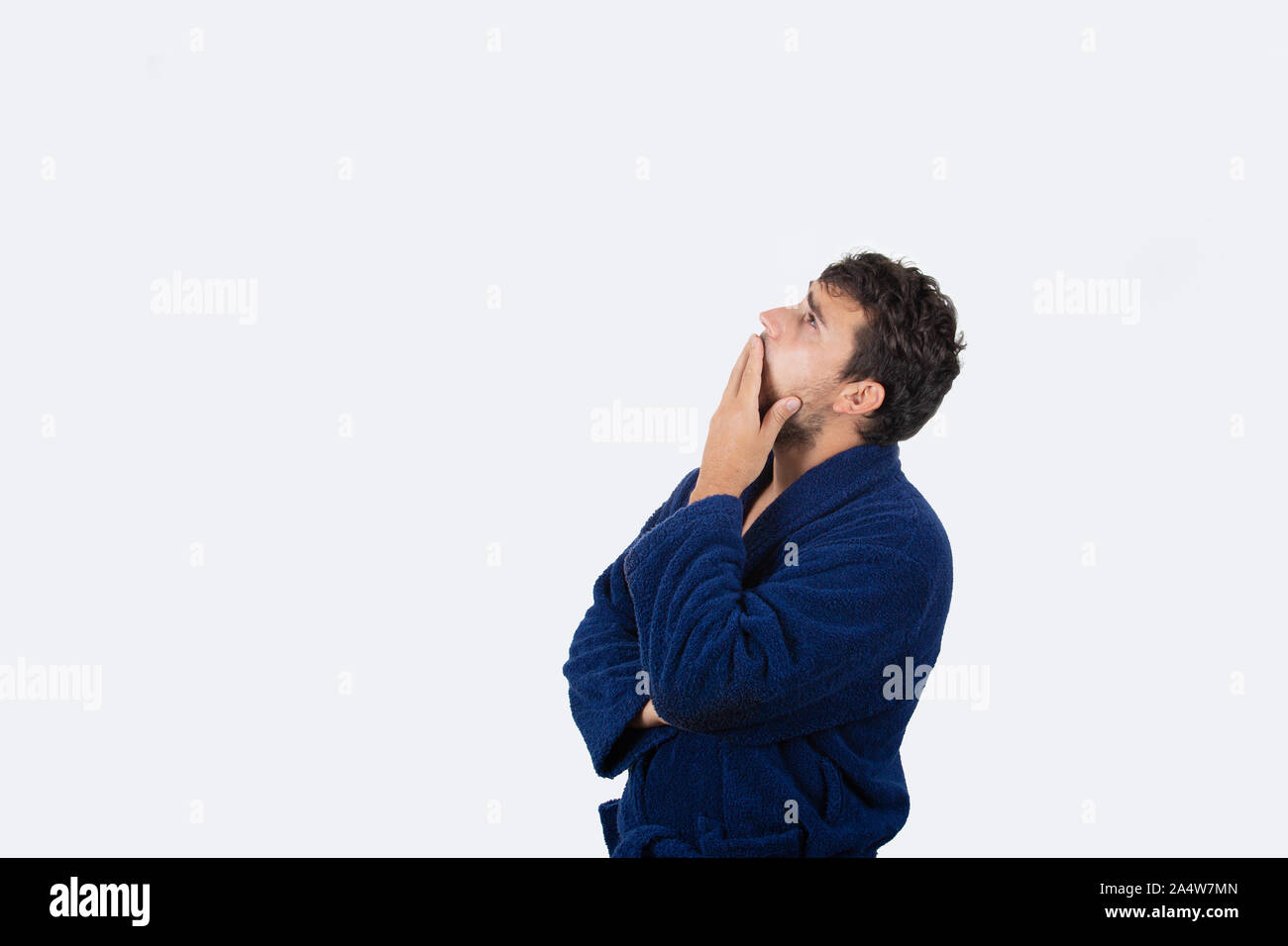 Sleepy young businessman yawning wearing blue bathrobe looking up,  feel tired needs to sleep isolated on white background. Stock Photo