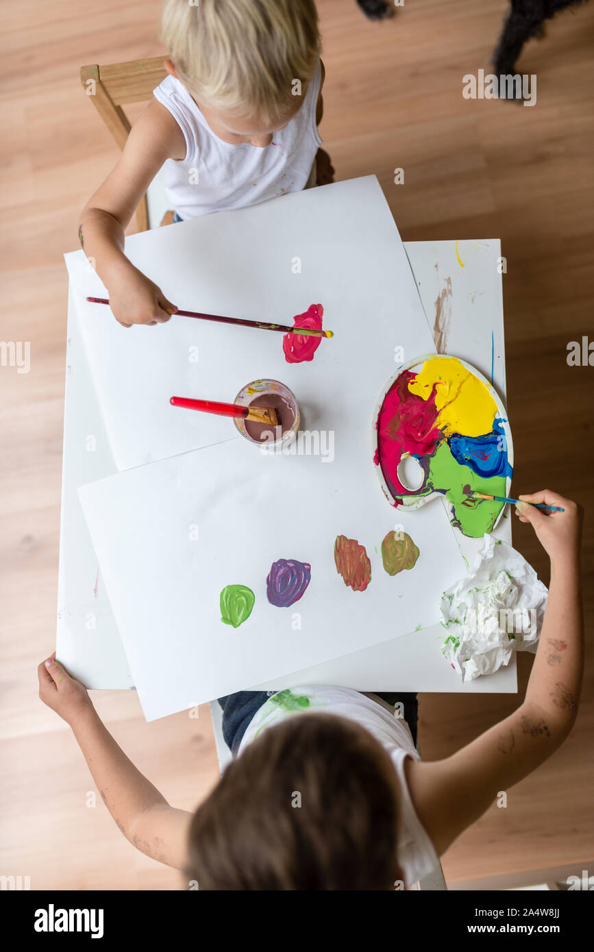 Top view of two children painting with watercolors with brush and a ...