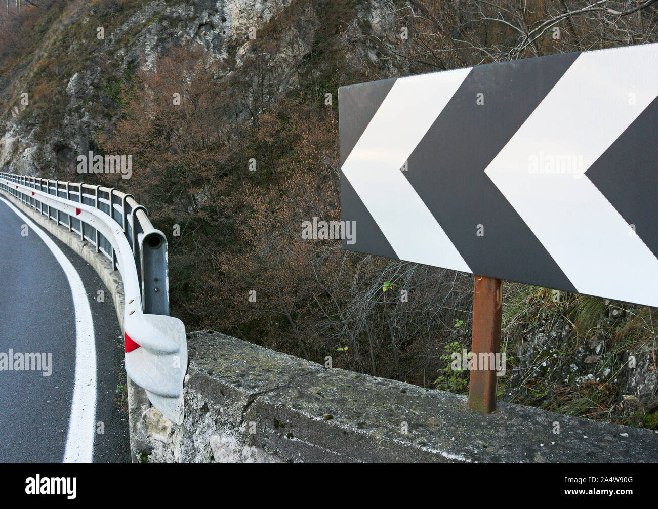 A left turn arrow sign ahead indicates a sharp turn in a mountain road Stock Photo