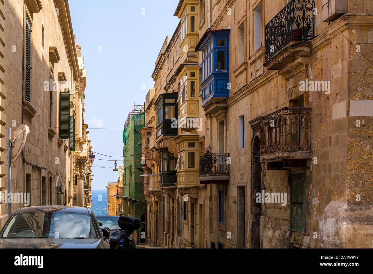 Residential house facade with traditional Maltese multicolored enclosed wooden balconies in Valletta, Malta, with sea at background. Stock Photo