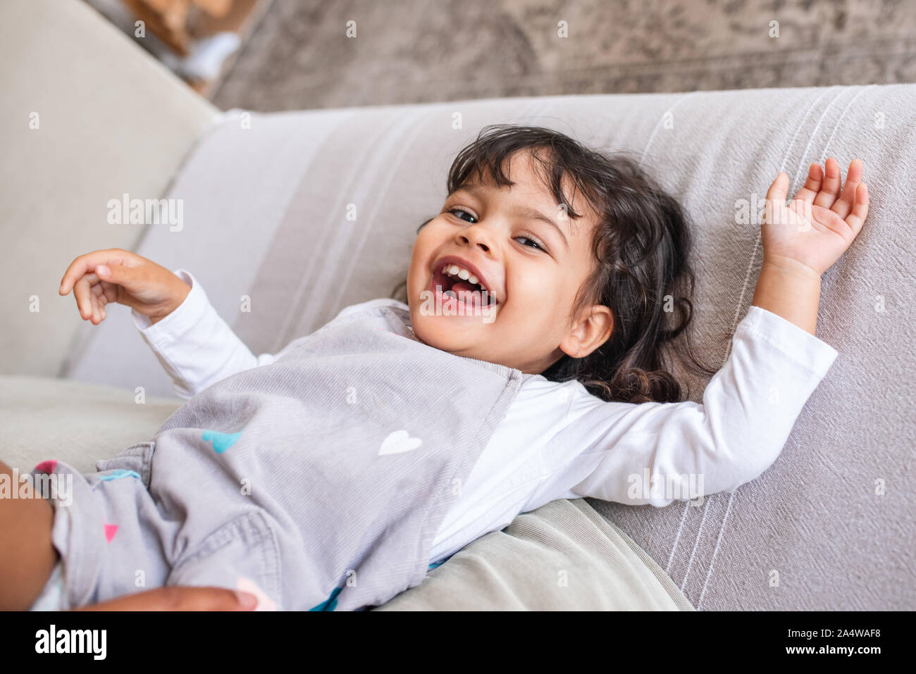 Laughing little girl playing on her living room sofa Stock Photo - Alamy