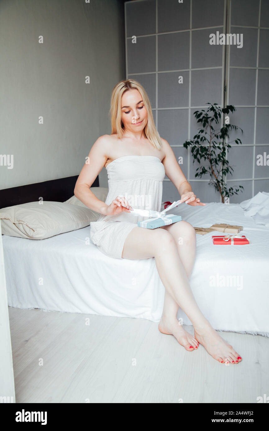 Woman blonde morning opens gifts for a holiday in the bedroom on the bed Stock Photo