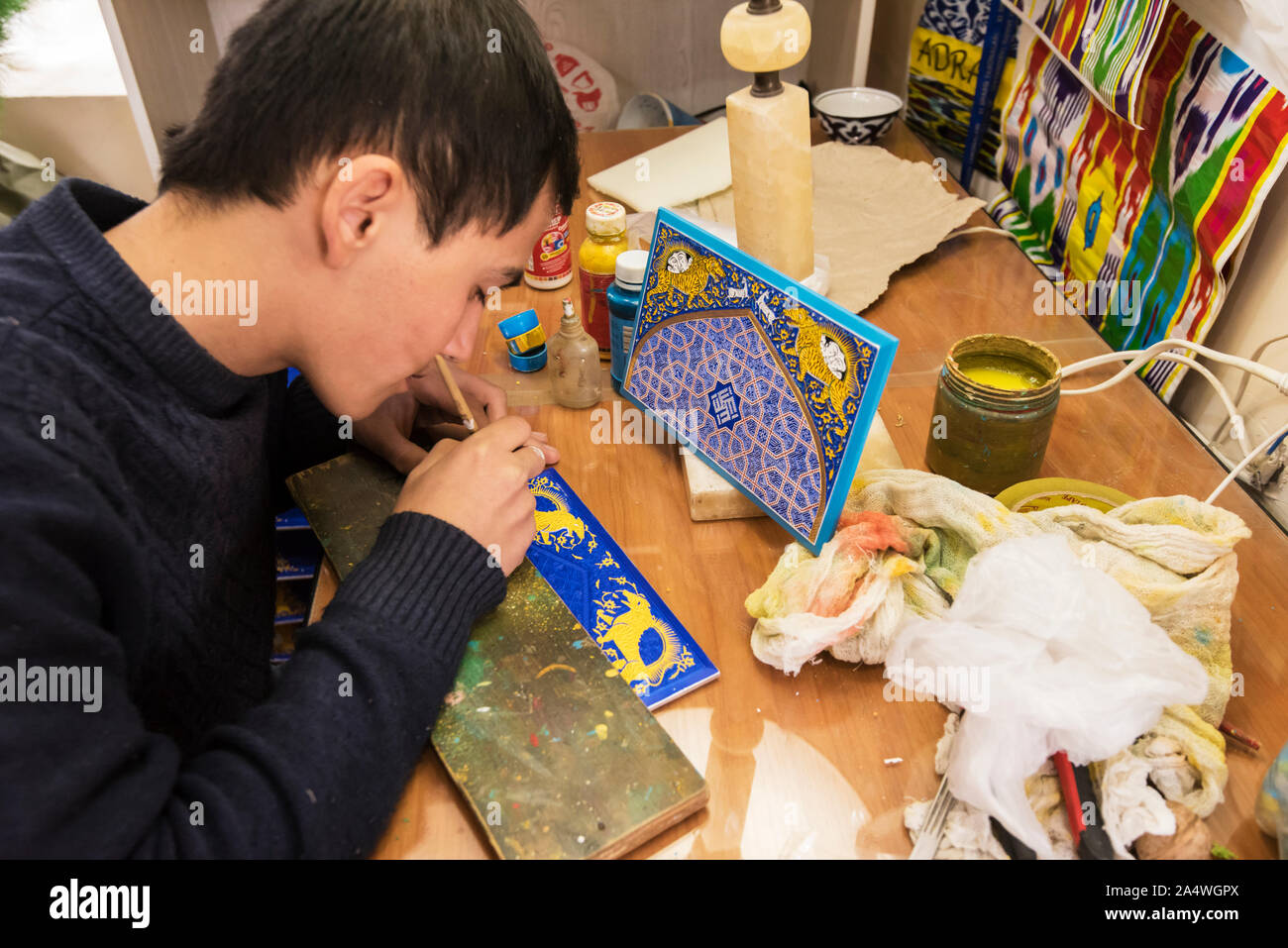 A boy working in the traditional art of painting. “Schastivaya ptitsa” (Happy Bird) Art Gallery, housed in a historical building of a wooden caravanse Stock Photo